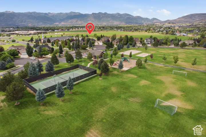 Expansive green space featuring a tennis court, playground, soccer goals, and volleyball courts, set against a mountain backdrop