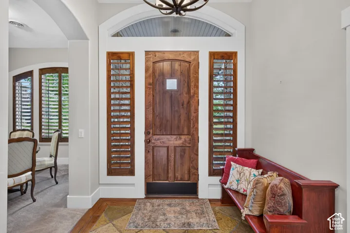 Arched transom window, wood-paneled entry door, sidelight windows with wood shutters, decorative overhead light fixture, and tile flooring with a wood border