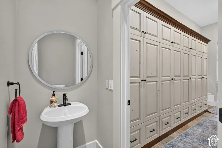 Pedestal sink with a black faucet, round wall mirror, and extensive custom cabinetry with dark hardware