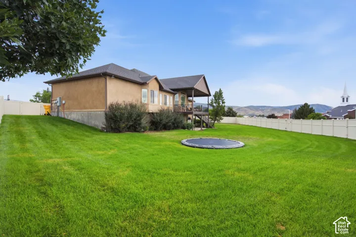 Expansive backyard featuring a lush lawn, privacy fencing, and a multi-level deck with covered porch