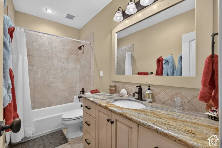 Bathtub with tiled surround, single vanity with an integrated sink, patterned countertop, and bronze-finish fixtures