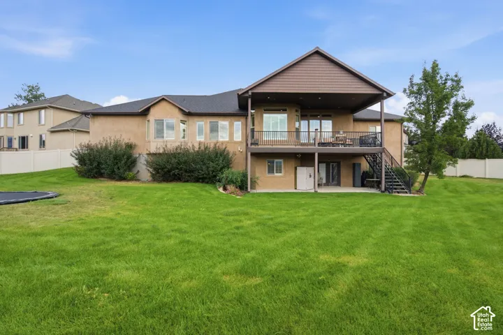 Expansive green lawn, stucco exterior, upper-level deck, covered lower patio, and mature landscaping
