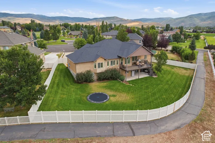 Expansive backyard featuring a manicured lawn, white vinyl fencing, and a multi-level deck with a lower patio