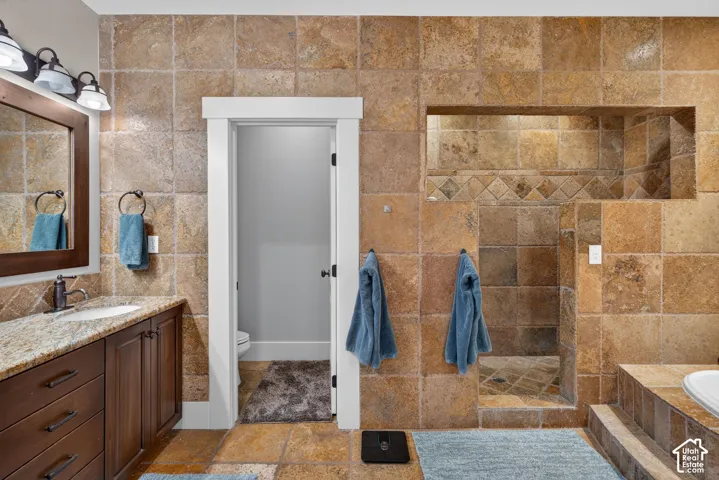 Tiled flooring and walls, a built-in shower niche, a vanity with a granite countertop, and a vessel sink