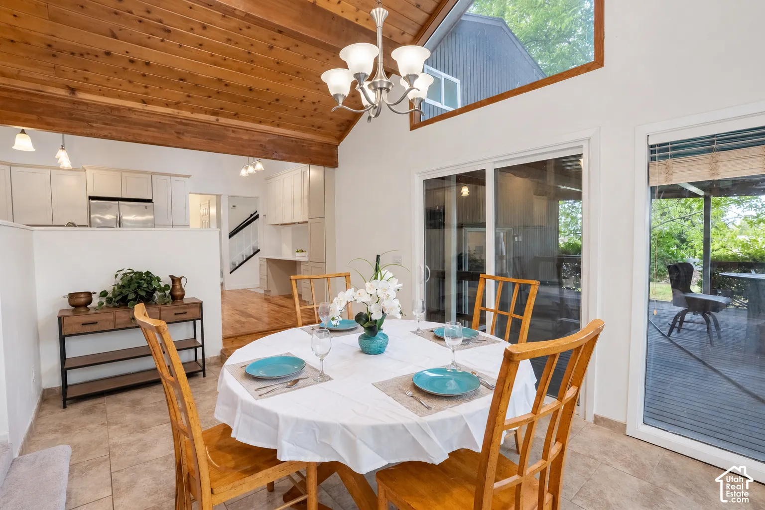 Vaulted wood-paneled ceiling with exposed beams, tiled flooring, chandelier lighting, and new paint and sliding door.