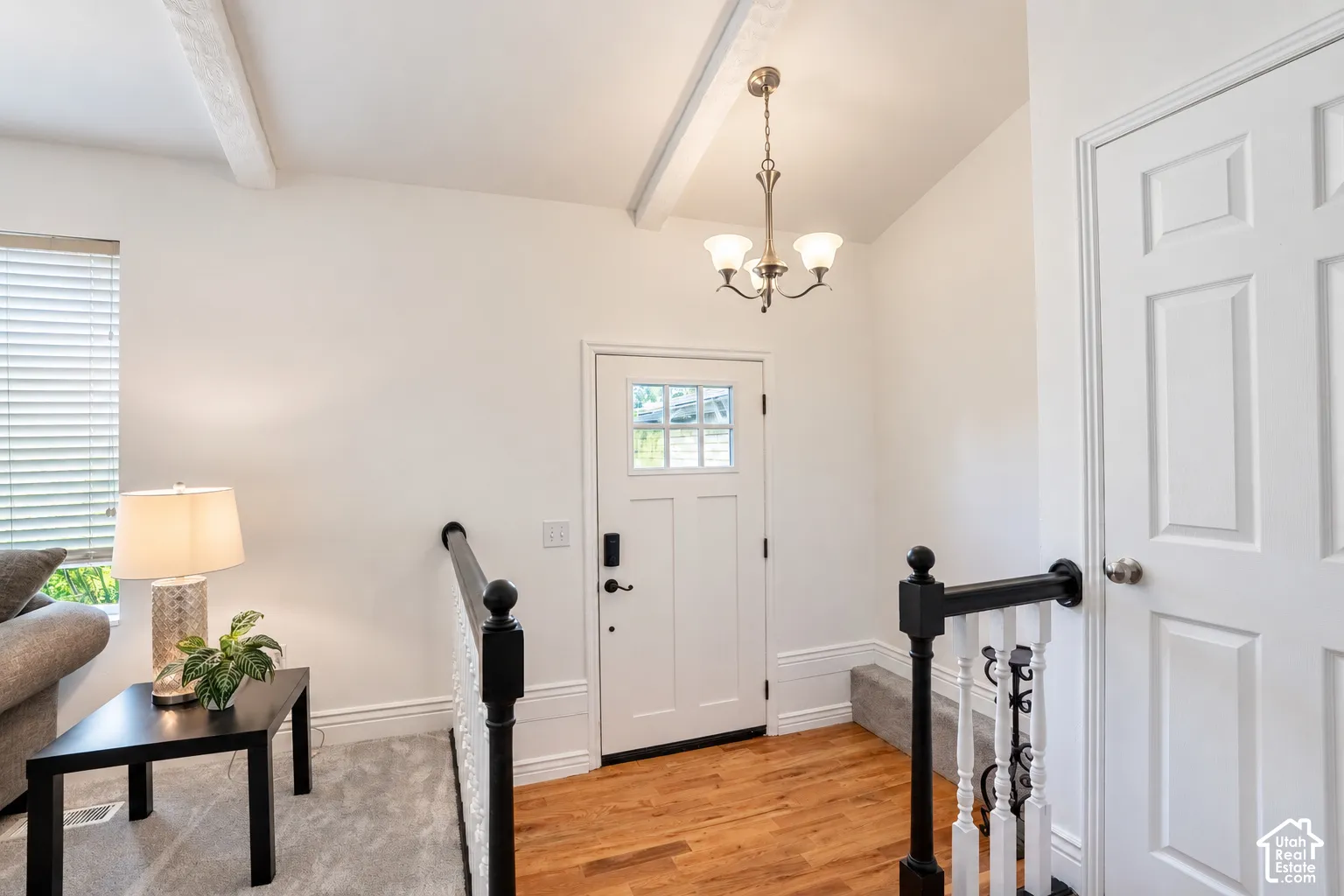 Vaulted ceiling with exposed beams, wood-finish flooring, white paneled door, and a decorative chandelier