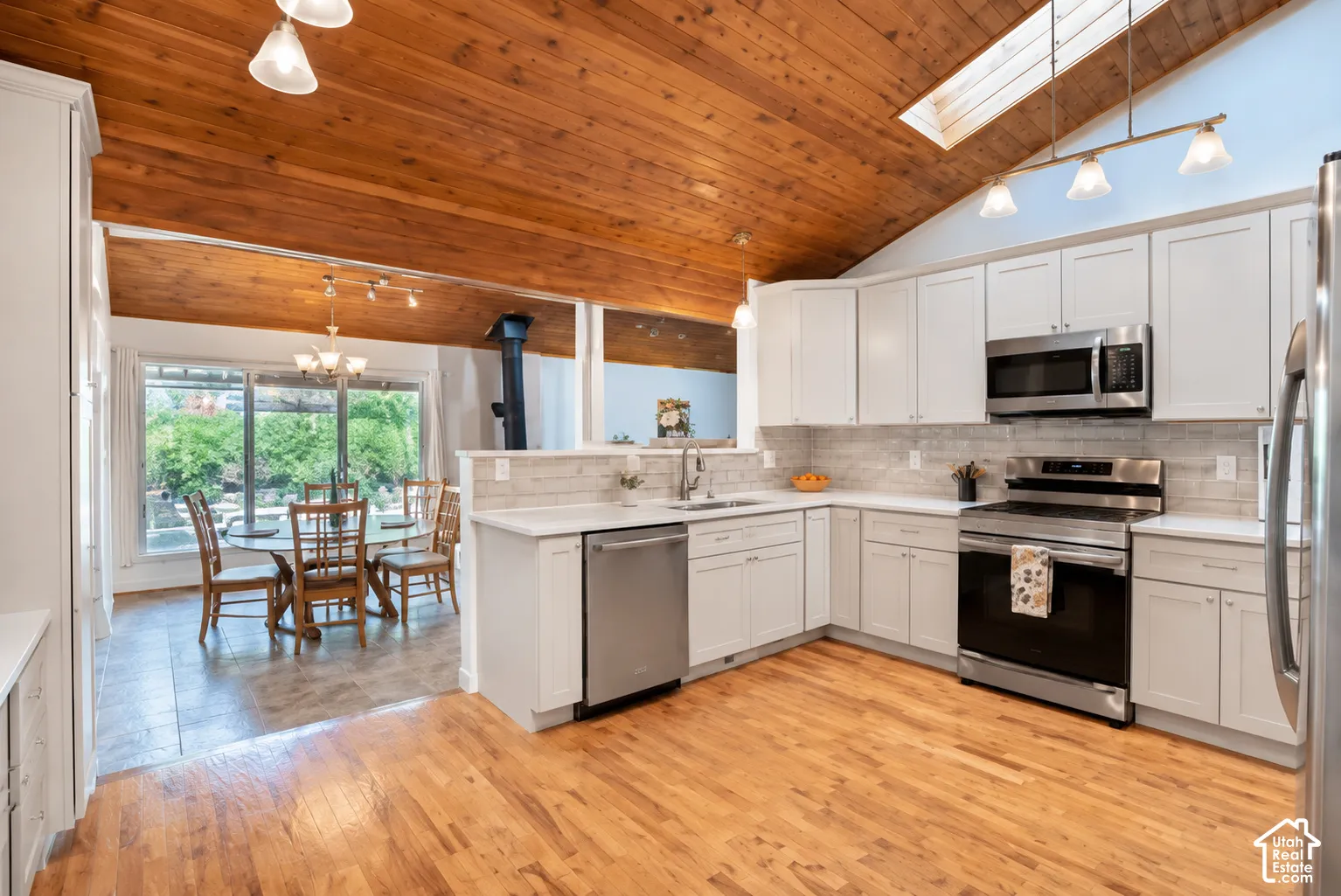 Vaulted wood-paneled ceiling, skylight, stainless steel appliances, white cabinetry, and wood-finish flooring