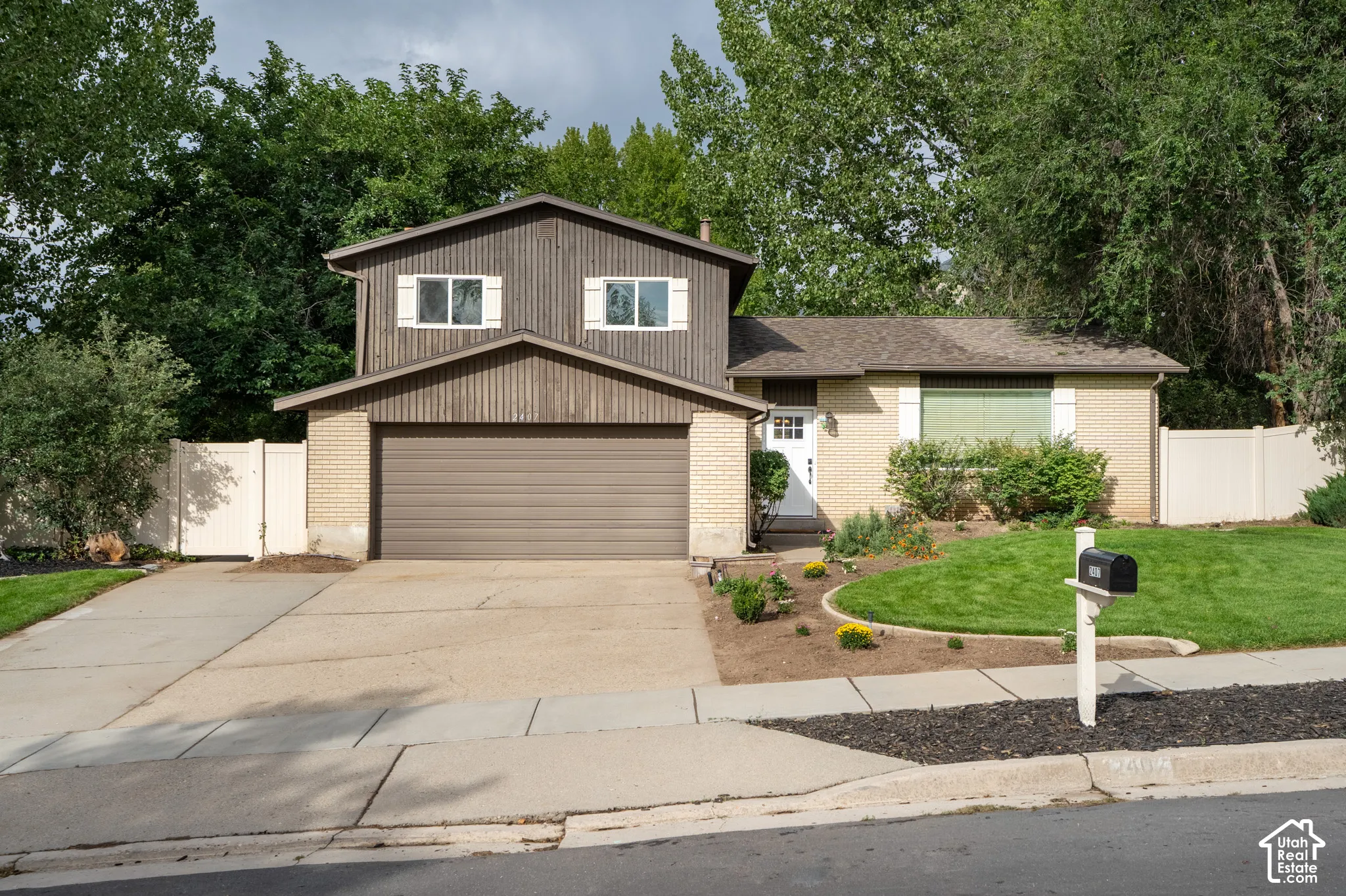 Brick and wood-sided exterior featuring an attached garage, paved driveway, mature landscaping, and new entry door