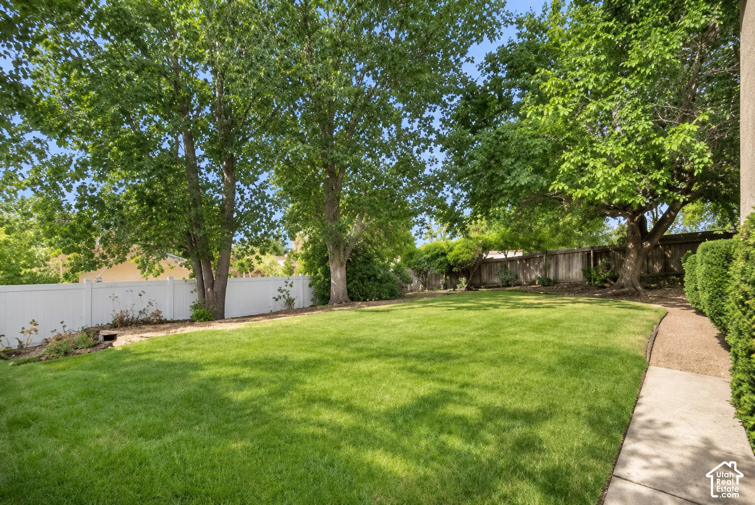 Expansive lawn area with mature trees, white panel fencing, and a paved pathway