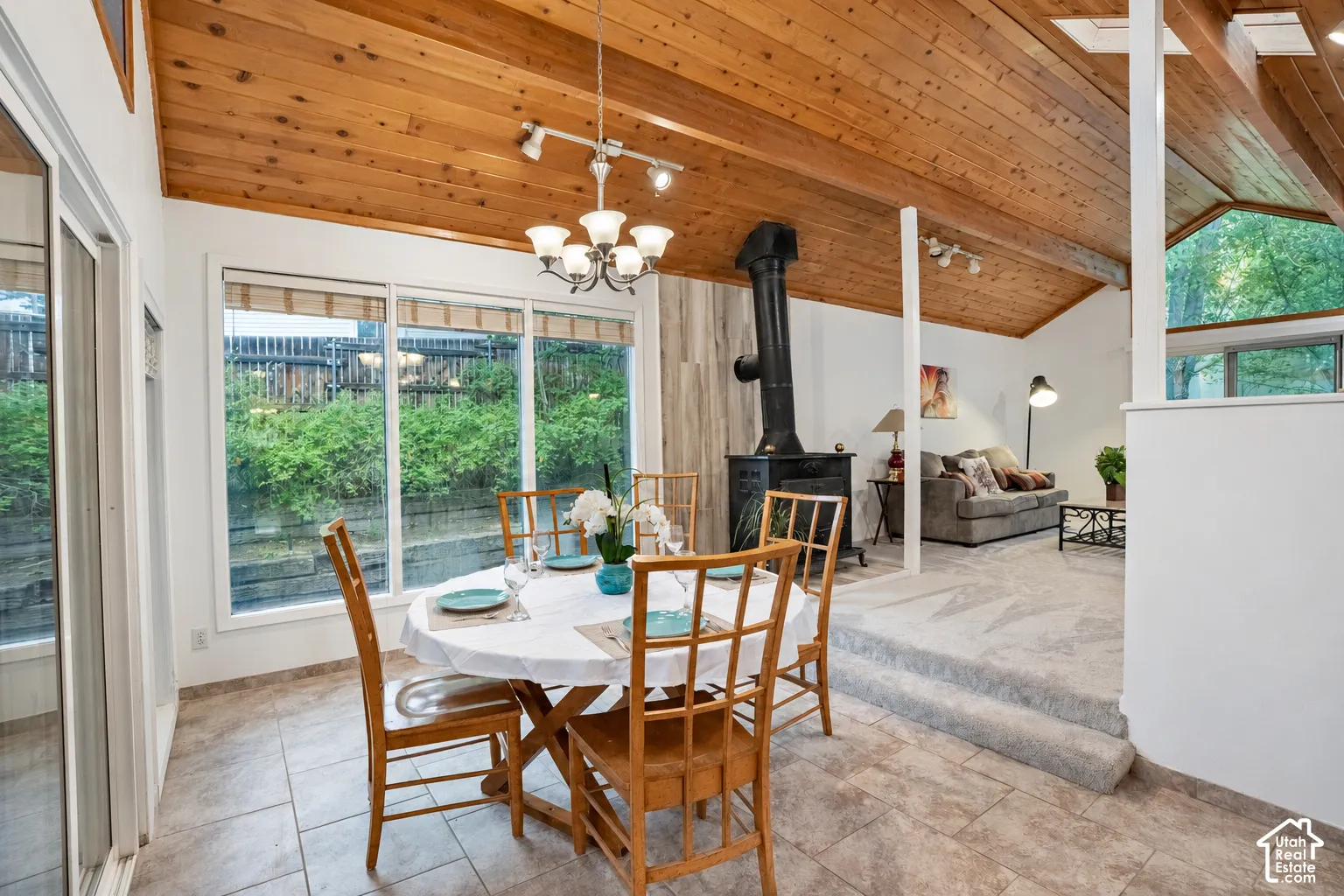 Vaulted wood-paneled ceiling, large windows, tiled flooring, built-in wood-burning stove, and a stepped transition to a carpeted area