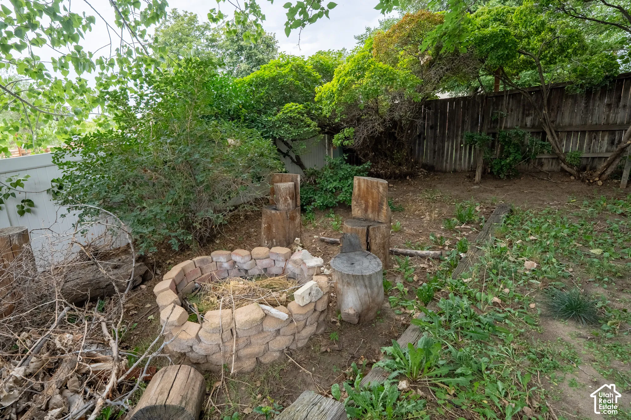 Backyard featuring a stone-lined fire pit, natural wood seating, a wood privacy fence, and mature foliage