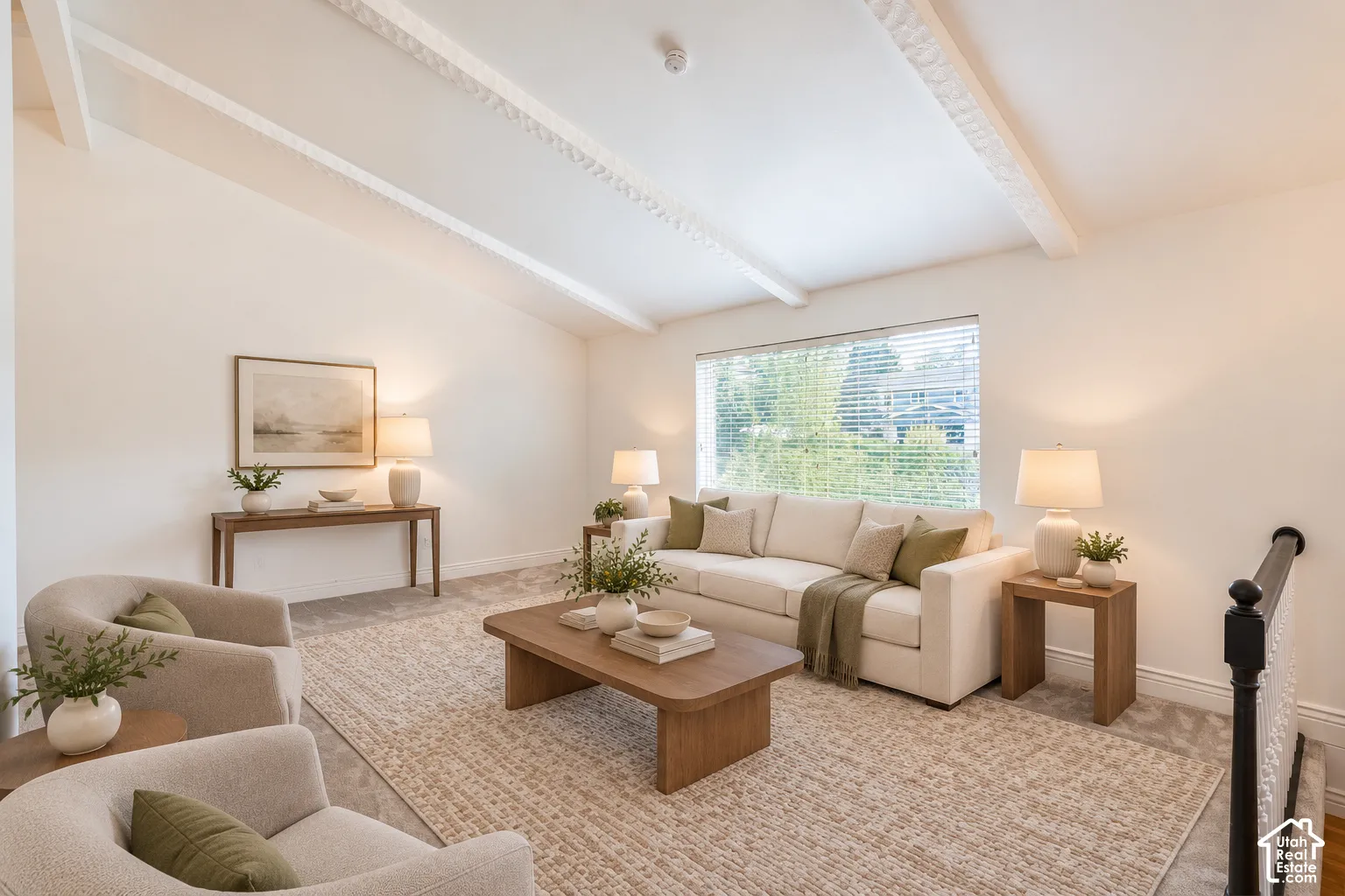 Vaulted ceiling with decorative beams, large window with blinds, carpeted flooring, and a black baluster railing