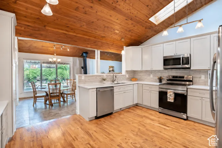 Vaulted wood-paneled ceiling, skylight, stainless steel appliances, white cabinetry, and wood-finish flooring