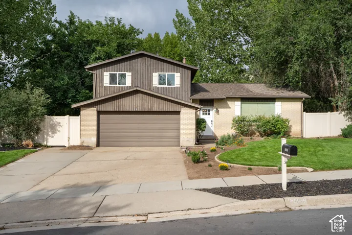 Brick and wood-sided exterior featuring an attached garage, paved driveway, mature landscaping, and new entry door