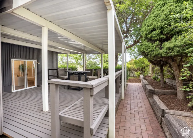 Covered outdoor patio with sliding glass door access to the interior, brick paver walkway, and tiered landscaping with mature trees
