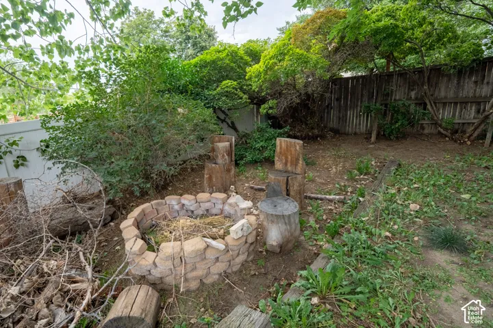 Backyard featuring a stone-lined fire pit, natural wood seating, a wood privacy fence, and mature foliage