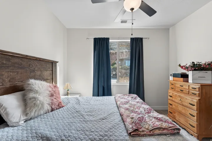 Window with dark drapery panels, ceiling fan with integrated lighting, wood-finish headboard, and neutral wall paint