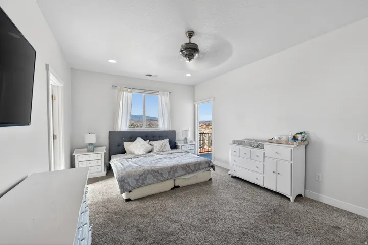 Spacious room featuring carpeting, white walls, a ceiling fan, a large window, and an exterior balcony