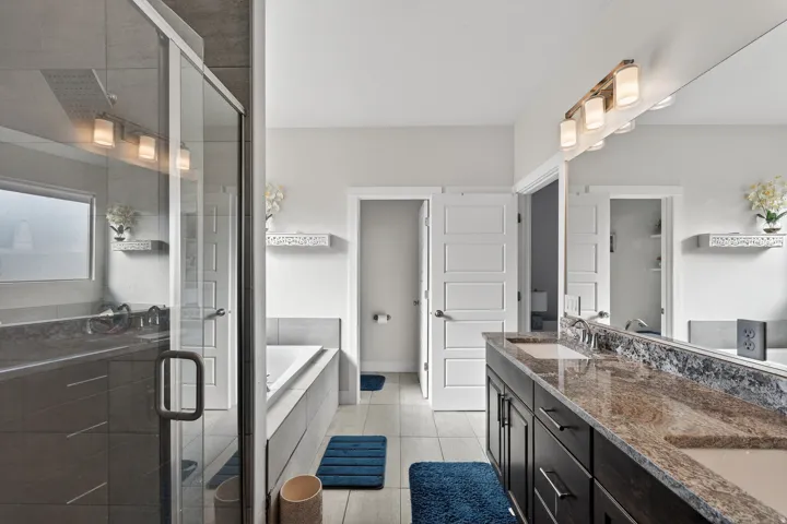 Dual vanity with stone countertop, built-in soaking tub, glass-enclosed shower, and recessed lighting