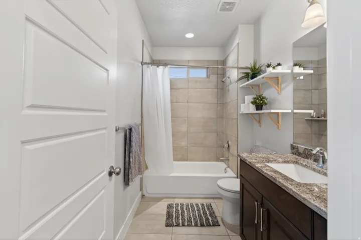 Bathroom featuring a combination shower and tub, tiled surround, window, dark wood-finish vanity with a light-colored countertop, and a recessed ceiling light
