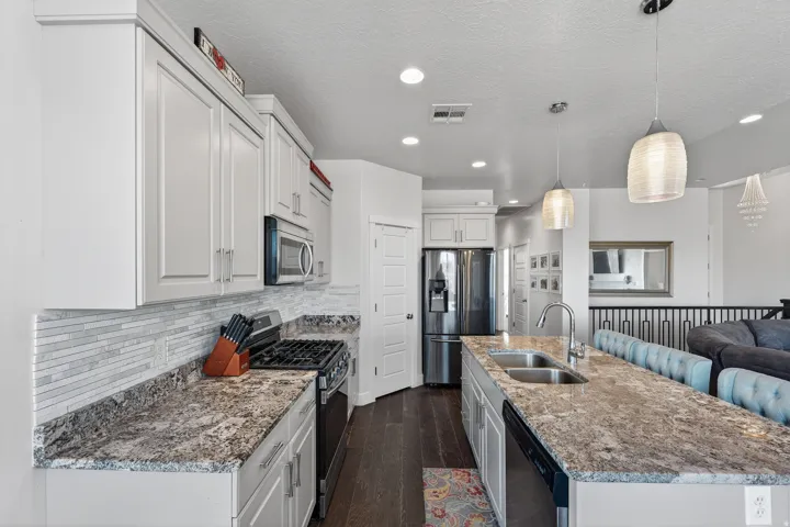 Kitchen featuring white cabinetry, stone-look countertops, a tile backsplash, stainless steel appliances, and an island with a double basin sink