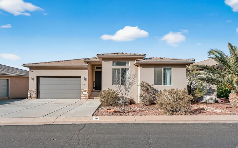 Stucco exterior with stone accents, attached garage, concrete driveway, and covered entry