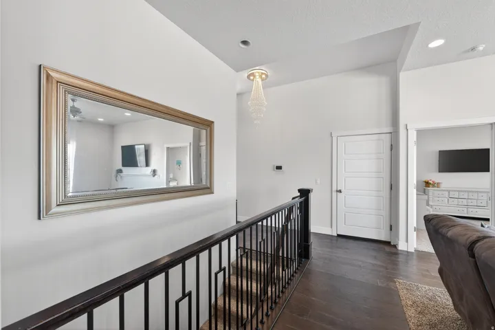 Dark wood-finish flooring with a contrasting white wall, featuring a modern five-panel door, black metal railing, and a crystal chandelier