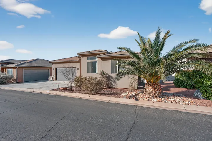 Stucco exterior with a tiled roof, front landscaping featuring a large palm tree, and an attached garage with a paved driveway