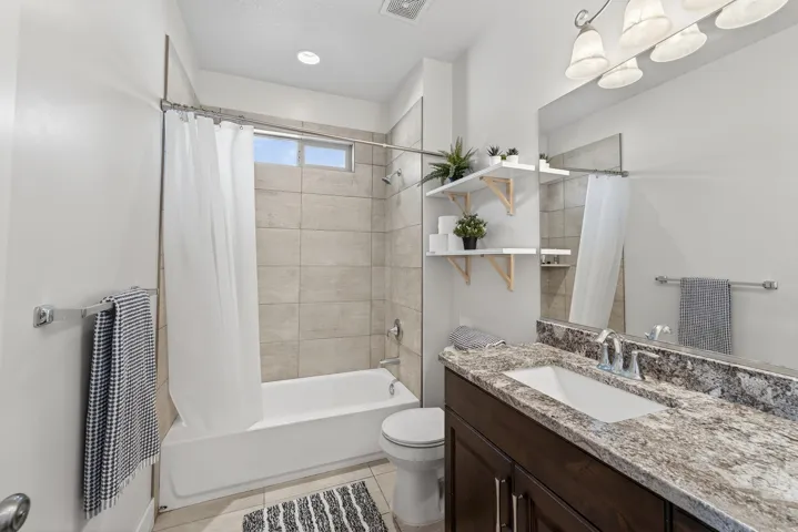 Bathroom featuring a shower-tub combination with large format tile surround, a single vanity with a stone countertop, an undermount sink, and wood-finish cabinetry
