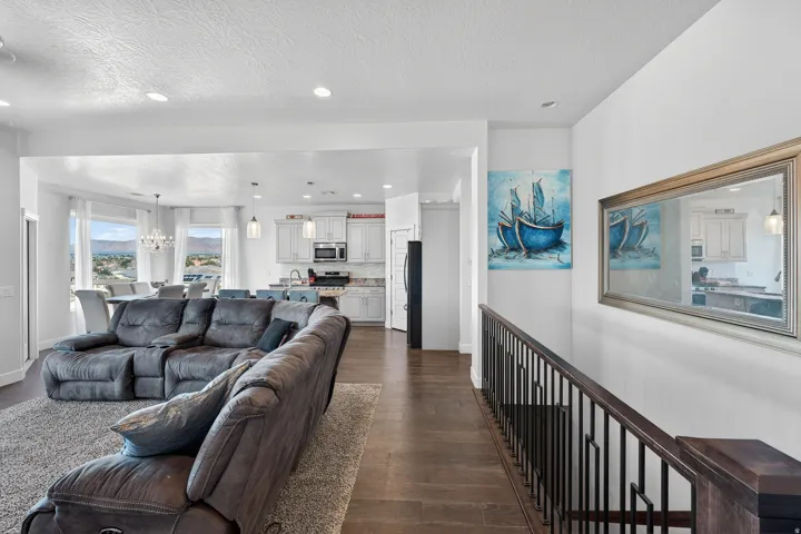 Open-concept living space featuring wood-finish flooring, recessed lighting, white walls, and a staircase with dark wood and metal railing