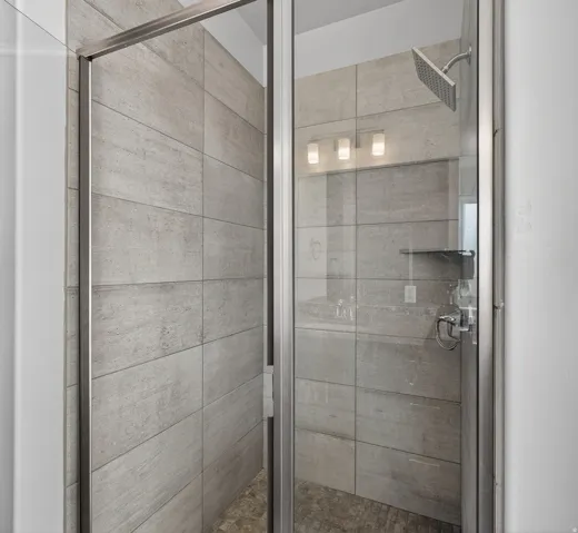 Glass-enclosed shower with large-format tile surround, rain shower head, and built-in shelving