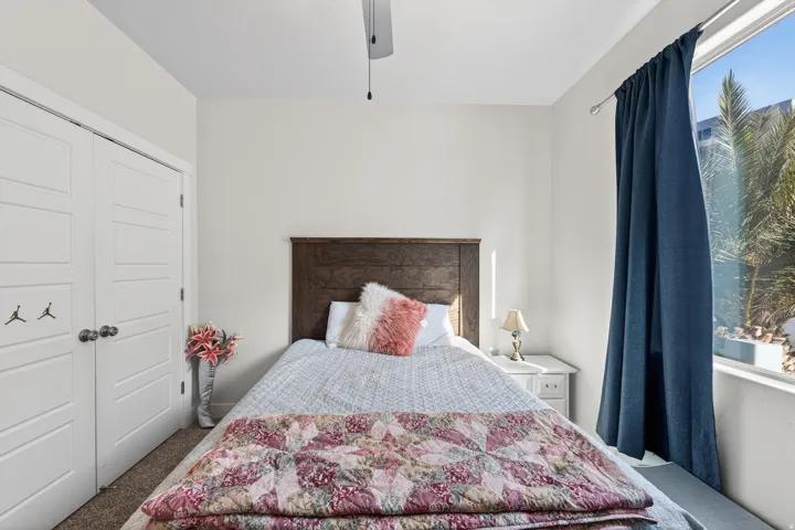 White paneled closet doors, wood headboard, ceiling fan, and large window with exterior foliage