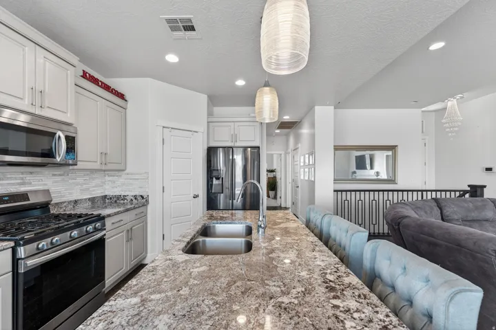 Kitchen featuring light-toned cabinetry, stainless steel appliances, a mosaic tile backsplash, a double basin sink, and pendant lighting