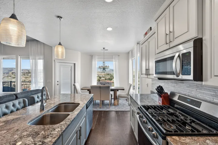 Kitchen featuring granite countertops, wood-finish flooring, stainless steel appliances, white cabinetry, and a tile backsplash
