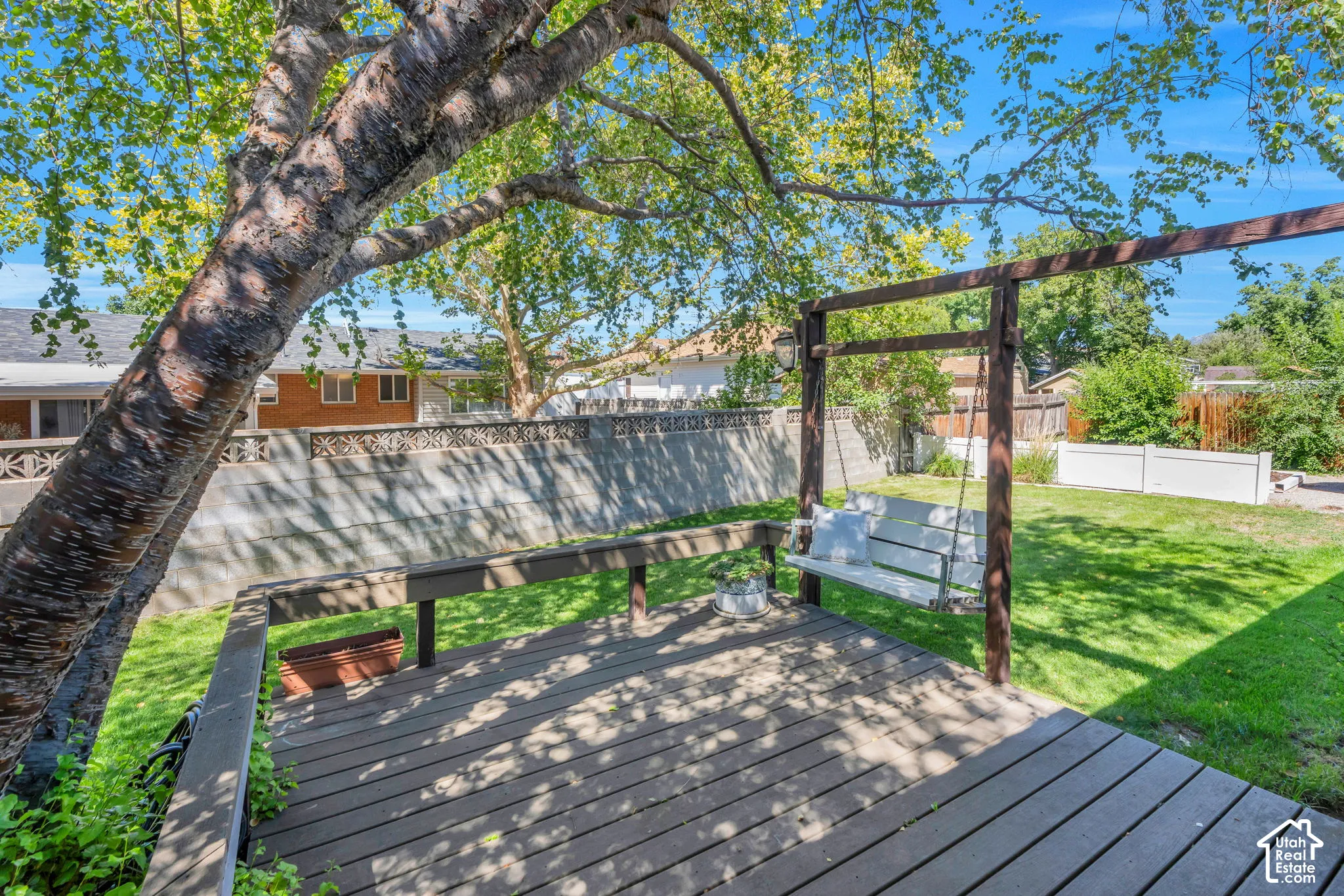 Expansive wood-finish deck with integrated swing structure, mature shade tree, and surrounding privacy fence