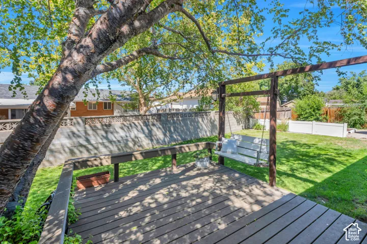 Expansive wood-finish deck with integrated swing structure, mature shade tree, and surrounding privacy fence