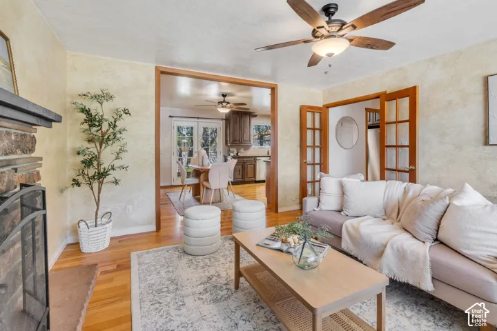 Hardwood flooring throughout, stone-clad fireplace, ceiling fan with integrated lighting, wood-framed French doors, and a wood-trimmed doorway