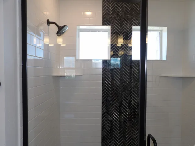Shower enclosure featuring white subway tile, dark herringbone accent tile, and a matte black shower head