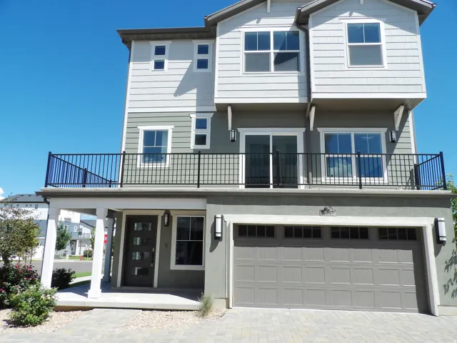 Multi-level exterior with a two-car garage, upper-level balcony with black railing, and a covered entry