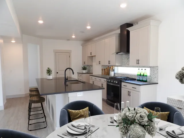 Kitchen featuring a large island with an undermount sink, pendant lighting, built-in cabinetry, modern range, and a tiled backsplash