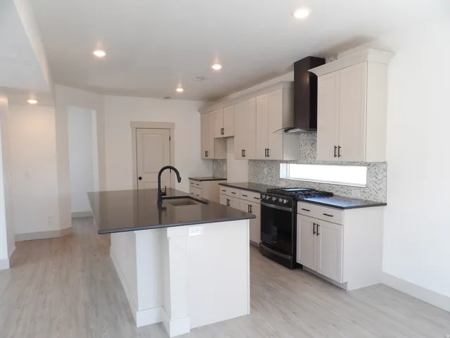Kitchen featuring a large island with sink, dark countertops, light cabinetry, and stainless steel appliances