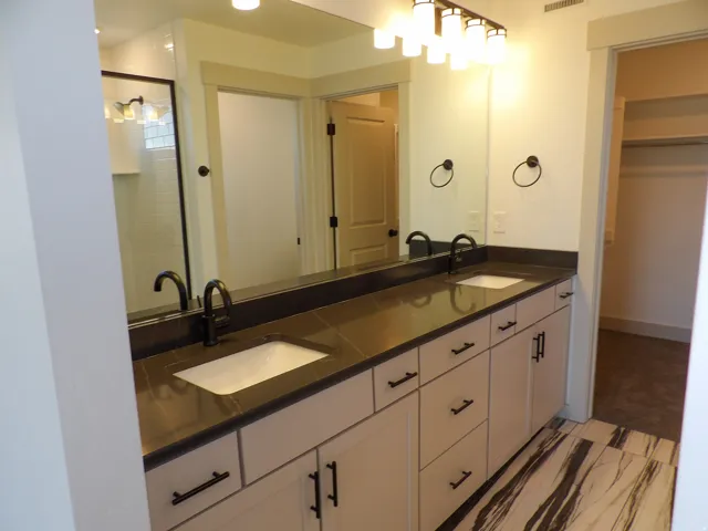 Spa-inspired primary bathroom featuring a lengthy vanity with dual rectangular vessel sinks, matte black hardware, and an expansive dark countertop