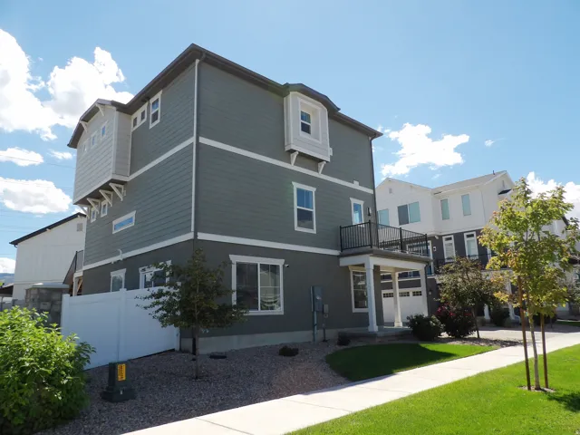 Contemporary exterior featuring gray siding, white trim, a second-story balcony with metal railing, an attached garage, and a white privacy fence