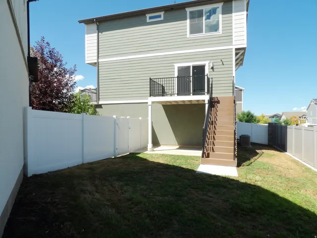 Exterior featuring horizontal siding, a private balcony with metal railing, an outdoor staircase, a concrete patio, and a privacy fence