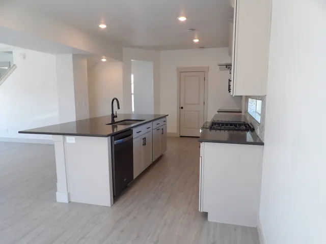 Kitchen featuring light-toned cabinetry, dark countertops, a center island with sink, and wood-finish flooring