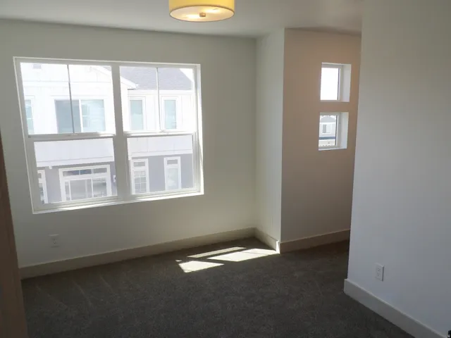 Wall-to-wall carpeted flooring, large window with white frame, white painted walls, and overhead flush mount lighting