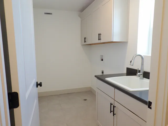 White shaker cabinetry with matte black hardware, integrated sink, dark countertop, and light-toned tile flooring