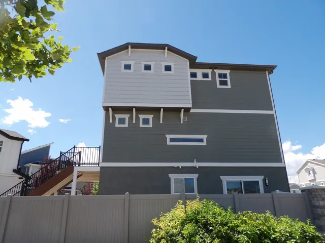 Multi-level exterior with mixed siding, an upper deck with metal railings, and a privacy fence