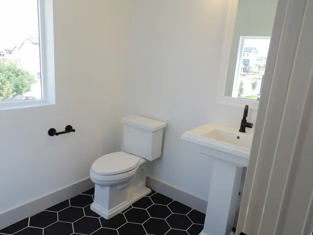 White pedestal sink with a matte black faucet, black hexagonal floor tiles, and a white framed mirror