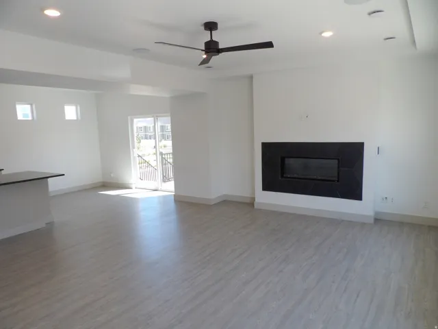 Spacious living area featuring light wood-finish flooring, a modern electric fireplace with dark hexagonal tile surround, and a ceiling fan